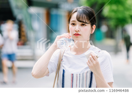 A young woman cools herself down with a plastic bottle during the heatwave A young woman cools herself down with a plastic bottle during the heatwave 116946486