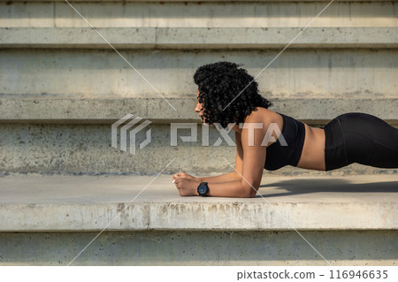 Curly-haired athletic woman standing in a plank Curly-haired athletic woman standing in a plank 116946635
