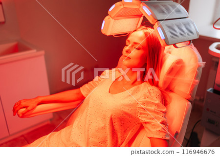 High-angle view of relaxed young woman having non-invasive type of phototherapy in medical clinic during hair treatment. Blonde female lying on chair having LED light hair photodynamic therapy. High-angle view of relaxed young woman having non-invasive type of phototherapy in medical clinic during hair treatment. Blonde female lying on chair having LED light hair photodynamic therapy. 116946676