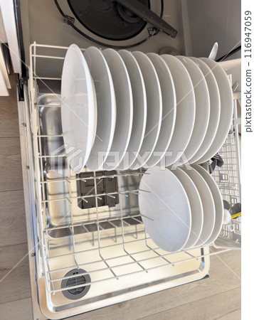 This image showcases a dishwasher filled with clean white dishes, neatly arranged in rows. Plates are stacked upright, while bowls are placed in the lower rack. The organized layout suggests 116947059