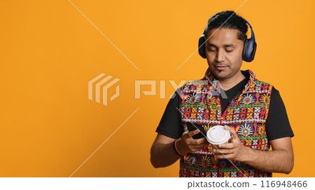 Joyous man listening music, having fun dancing, enjoying hot beverage. Upbeat person wearing headphones, doing funky movements, drinking coffee, studio background, camera A Joyous man listening music, having fun dancing, enjoying hot beverage. Upbeat person wearing headphones, doing funky movements, drinking coffee, studio background, camera A 116948466