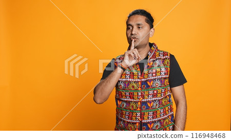 Annoyed indian man doing shushing hand gesturing, irritated by noise, having negative mood. Person placing finger on lips, doing quiet sign gesture, studio background, camera B 116948468