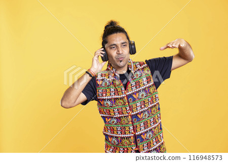 Joyous man playing electronic music, having fun moving on rhythm, pretending to use turntables. Happy DJ wearing headphones producing beats during relaxation time, studio backdrop Joyous man playing electronic music, having fun moving on rhythm, pretending to use turntables. Happy DJ wearing headphones producing beats during relaxation time, studio backdrop 116948573