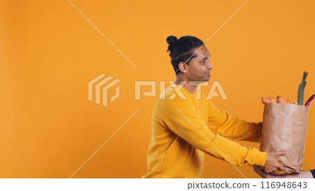 Friendly upbeat pizza delivery employee giving takeaway order to client paying with credit card. Asian man offering groceries order and digital payment method to customer, studio background, camera B Friendly upbeat pizza delivery employee giving takeaway order to client paying with credit card. Asian man offering groceries order and digital payment method to customer, studio background, camera B 116948643