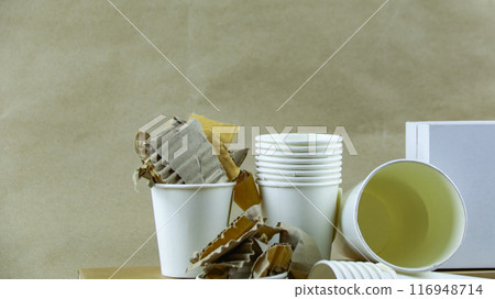 White paper coffee cup, used paper, and cardboard box on a brown surface, awaiting recycling. White paper coffee cup, used paper, and cardboard box on a brown surface, awaiting recycling. 116948714