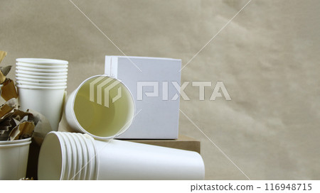 White paper coffee cup, used paper, and cardboard box on a brown surface, awaiting recycling. 116948715