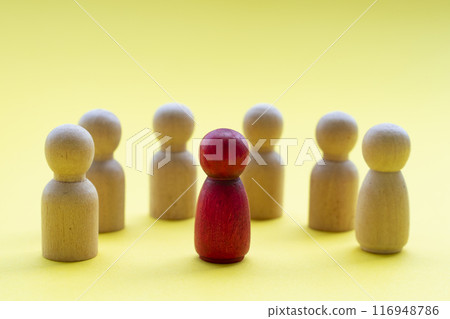 A red wooden figure surround by other wooden figures representing either someone is a leader or someone being discriminated 116948786