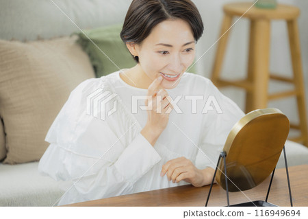 Middle-aged woman looking in the mirror in the living room 116949694