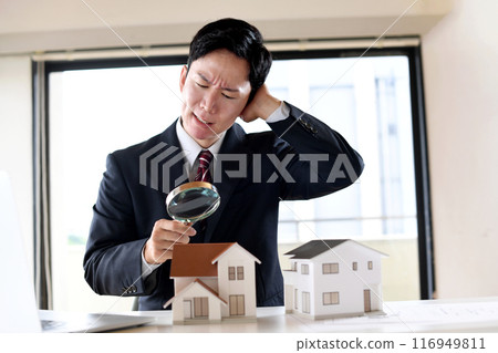 A worried man in a suit looking at a model house through a magnifying glass A worried man in a suit looking at a model house through a magnifying glass 116949811
