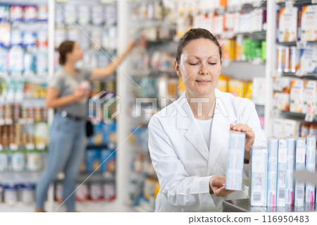 In pharmacy, woman chemist makes out showcase with warming analgesic ointments In pharmacy, woman chemist makes out showcase with warming analgesic ointments 116950483