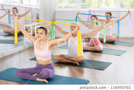 Group Pilates classes - woman doing body stretching using elastic bands in gym Group Pilates classes - woman doing body stretching using elastic bands in gym 116950702