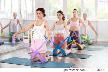 Women are doing stretching exercise with resistance bands in gym. Teamwork, good mood and healthy lifestyle concept Women are doing stretching exercise with resistance bands in gym. Teamwork, good mood and healthy lifestyle concept 116950796
