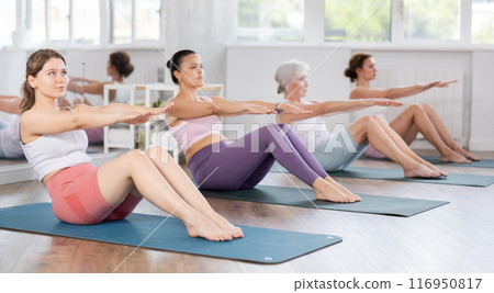 Athletic women doing pilates or aerobics - doing back exercises during group training in gym Athletic women doing pilates or aerobics - doing back exercises during group training in gym 116950817