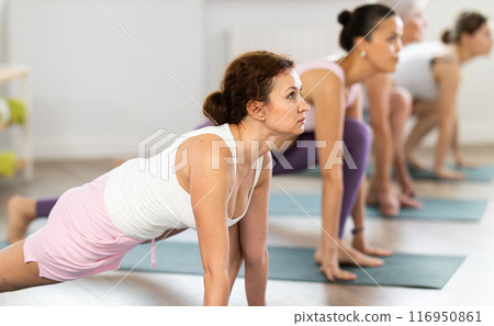 Woman performing Low Lunge Pose with group in yoga studio 116950861