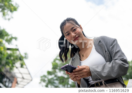 An attractive Asian businesswoman is standing outdoors in the city with a smartphone in her hand. An attractive Asian businesswoman is standing outdoors in the city with a smartphone in her hand. 116951629