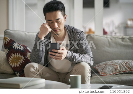 young asian adult man looking at cellphone at home young asian adult man looking at cellphone at home 116951892