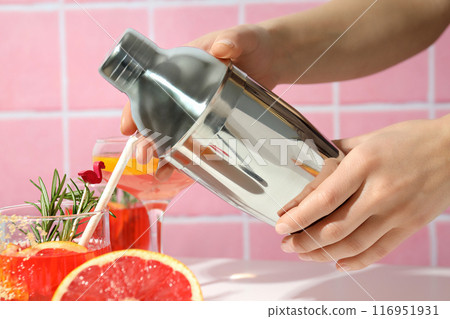 Shaker in hands and grapefruit cocktails on pink background, close up Shaker in hands and grapefruit cocktails on pink background, close up 116951931