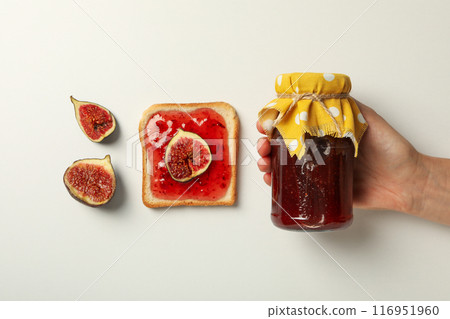 Figs, jar of jam in hand and piece of bread on white background, top view 116951960