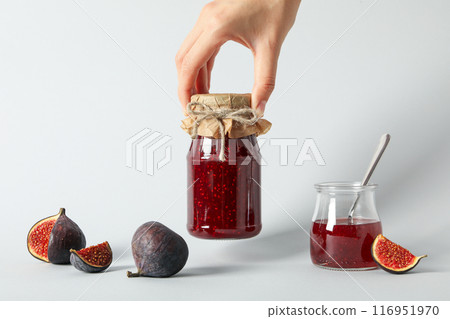 Figs and jars of jam in hand on white background 116951970