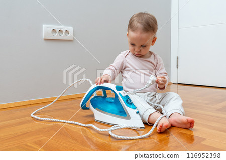 Baby playing with a household iron. Concept of bad toys in the house Baby playing with a household iron. Concept of bad toys in the house 116952398