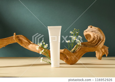 Unique template for designing of natural concept with frontal shot over dark blue texture. A white unlabeled cosmetic tube displayed on yellow countertop with a curved log and flowers in back Unique template for designing of natural concept with frontal shot over dark blue texture. A white unlabeled cosmetic tube displayed on yellow countertop with a curved log and flowers in back 116952926