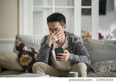 young asian man feeling eye fatigue as result of cellphone use 116953084