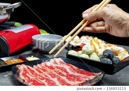 A hand holding chopsticks with a piece of meat on it 116953213
