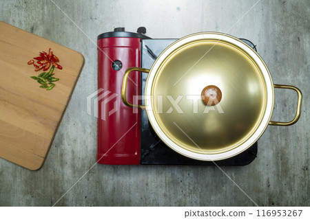 A red pot with a gold lid sits on top of a burner 116953267