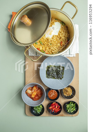 A pot of instant noodles with a lid on top of a wooden board with several bowls of food A pot of instant noodles with a lid on top of a wooden board with several bowls of food 116953294