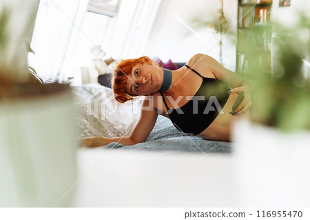 portrait of red-haired young woman lying on bed using mobile phone portrait of red-haired young woman lying on bed using mobile phone 116955470