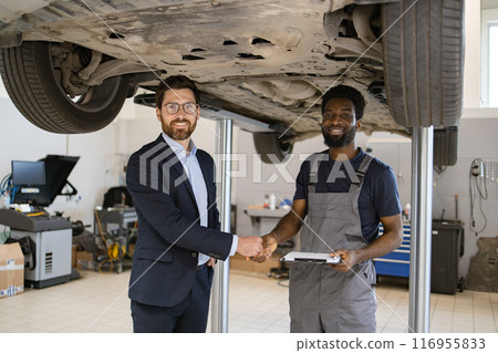 Businessman shaking hands with mechanic under car lift in garage 116955833