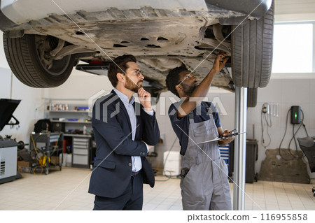 Mechanic explaining car inspection to business professional in auto repair shop Mechanic explaining car inspection to business professional in auto repair shop 116955858