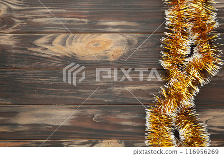 Christmas gold tinsel on brown wooden background. Christmas gold tinsel on brown wooden background. 116956269