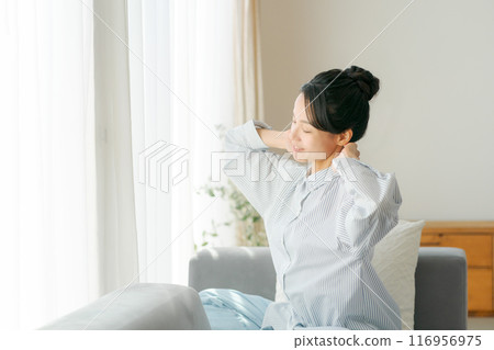 一名 30 多歲的女性在客廳伸展身體 一名 30 多歲的女性在客廳伸展身體 116956975