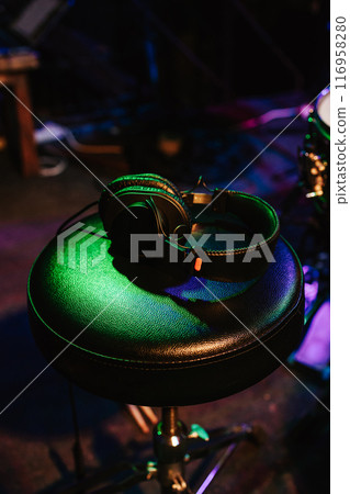 Preparing for a concert. Music headphones on the chair. Rock concert. DJs workplace. The musician's seat is flooded with green neon lights. Vertical photo Preparing for a concert. Music headphones on the chair. Rock concert. DJs workplace. The musician's seat is flooded with green neon lights. Vertical photo 116958280