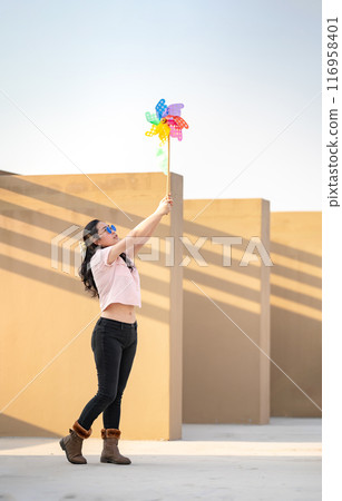 Asian woman posts and play Windmill Toy colourful rainbow colour on the building rooftop in sunset time. Asian woman posts and play Windmill Toy colourful rainbow colour on the building rooftop in sunset time. 116958401