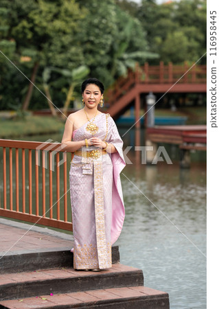 A woman in a traditional Thai costumes is standing on the wooden bridge while being taken a portrait photo shooting. A woman in a traditional Thai costumes is standing on the wooden bridge while being taken a portrait photo shooting. 116958445