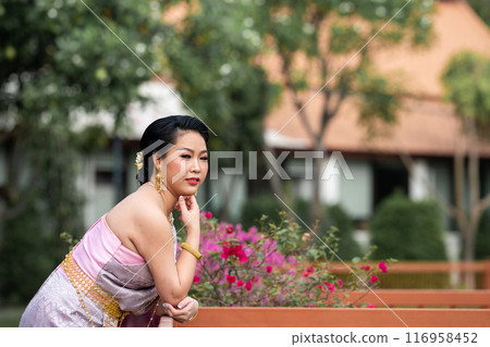 A woman in a traditional Thai costumes is standing on the wooden bridge while being taken a portrait photo shooting. A woman in a traditional Thai costumes is standing on the wooden bridge while being taken a portrait photo shooting. 116958452
