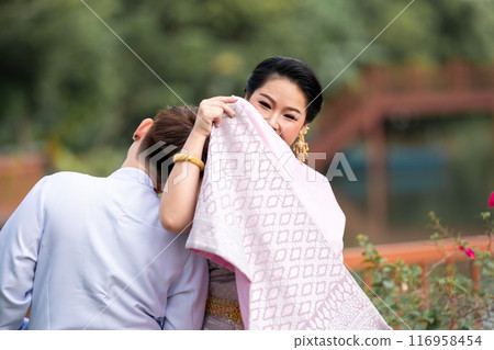 A woman in a traditional Thai costumes is standing on the wooden bridge while being taken a portrait photo shooting. 116958454