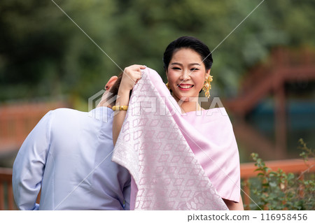 A woman in a traditional Thai costumes is standing on the wooden bridge while being taken a portrait photo shooting. 116958456