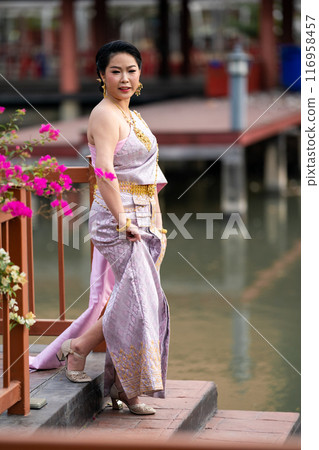 A woman in a traditional Thai costumes is standing on the wooden bridge while being taken a portrait photo shooting. A woman in a traditional Thai costumes is standing on the wooden bridge while being taken a portrait photo shooting. 116958457