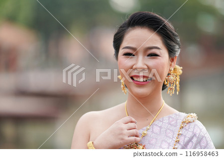A woman in a traditional Thai costumes is standing on the wooden bridge while being taken a portrait photo shooting. A woman in a traditional Thai costumes is standing on the wooden bridge while being taken a portrait photo shooting. 116958463