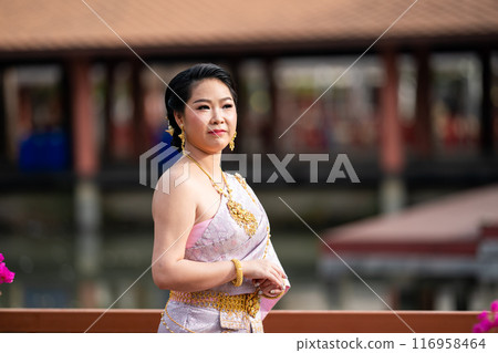 A woman in a traditional Thai costumes is standing on the wooden bridge while being taken a portrait photo shooting. A woman in a traditional Thai costumes is standing on the wooden bridge while being taken a portrait photo shooting. 116958464