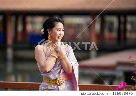 A woman in a traditional Thai costumes is standing on the wooden bridge while being taken a portrait photo shooting. 116958470