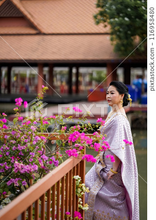 A woman in a traditional Thai costumes is standing on the wooden bridge while being taken a portrait photo shooting. 116958480