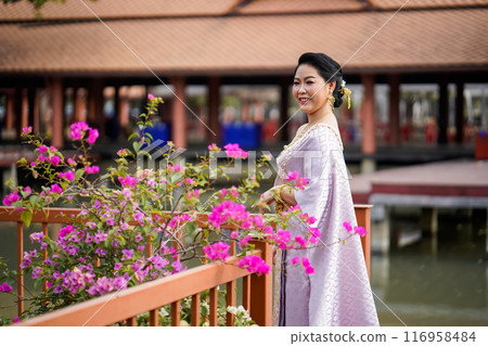 A woman in a traditional Thai costumes is standing on the wooden bridge while being taken a portrait photo shooting. A woman in a traditional Thai costumes is standing on the wooden bridge while being taken a portrait photo shooting. 116958484