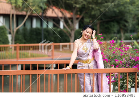 A woman in a traditional Thai costumes is standing on the wooden bridge while being taken a portrait photo shooting. 116958495