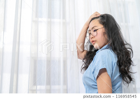 An Asian glasses woman in blue shirt poses by slicks her hair back in front of lightening curtain. An Asian glasses woman in blue shirt poses by slicks her hair back in front of lightening curtain. 116958545
