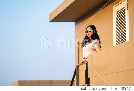 beautiful Asian woman is standing on the stair and looking over to the sky in the sunset time at rooftop of the building. beautiful Asian woman is standing on the stair and looking over to the sky in the sunset time at rooftop of the building. 116958547