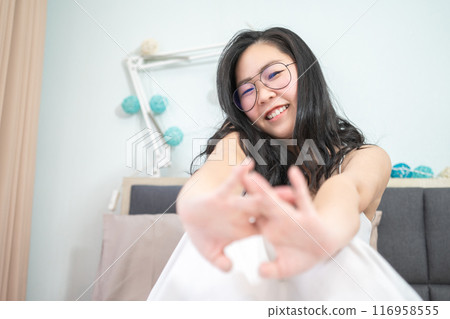 Asian young glasses woman stretches oneself on her bed in the morning. Asian young glasses woman stretches oneself on her bed in the morning. 116958555